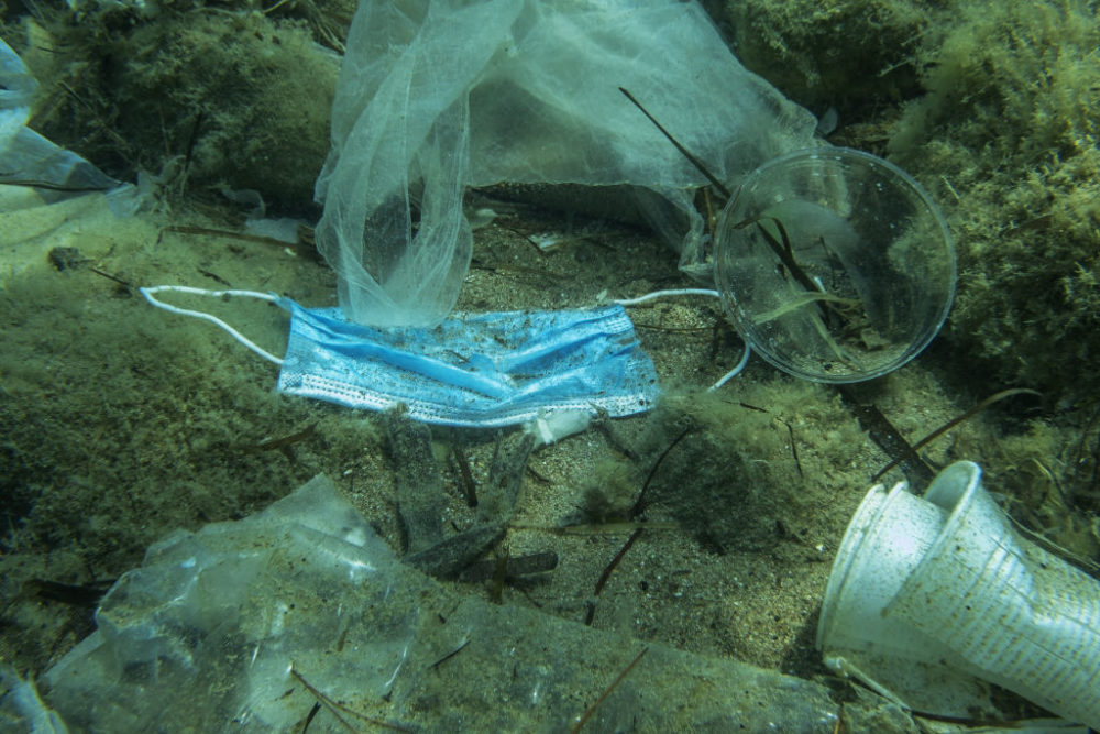 Discarded used medical face mask along with other plastic debris lies on the seabed. Becici, Budva Municipality, Montenegro